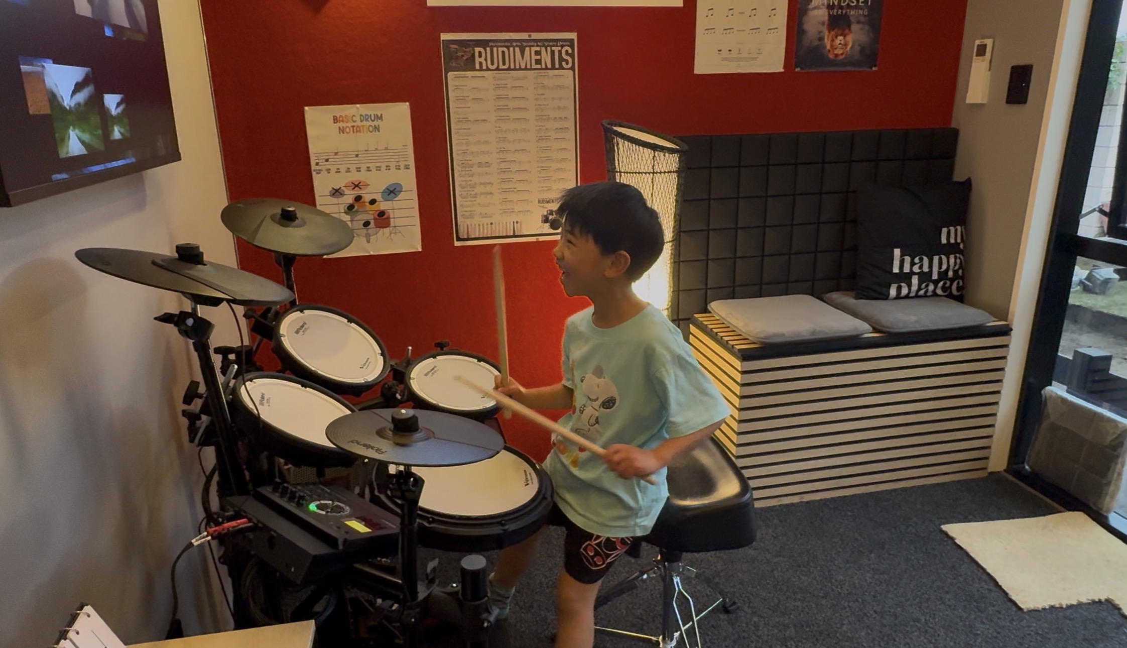 Student smiling while playing an electronic drum kit during a lesson