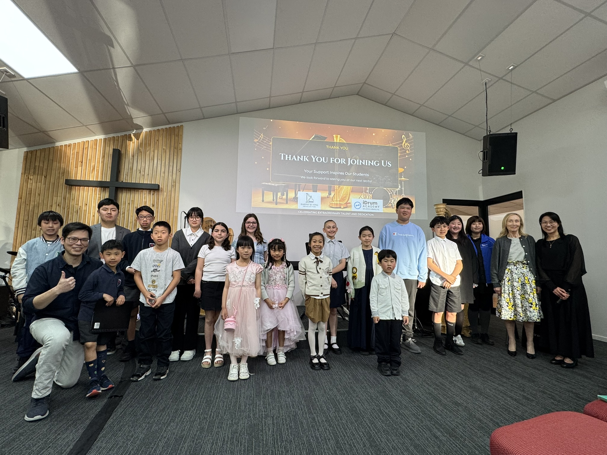 Students and families gathered after an iDrum Academy recital with a thank-you slide on screen